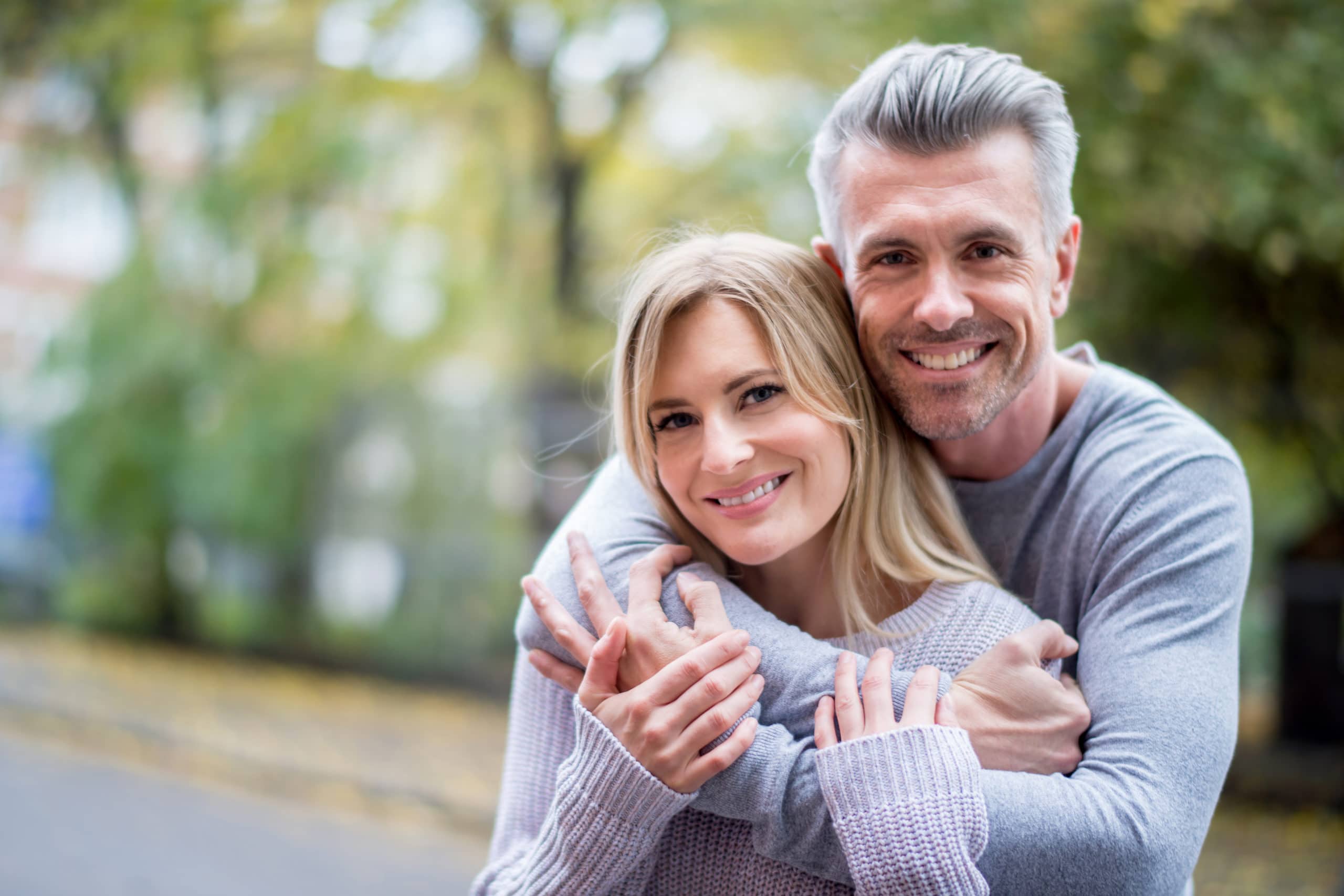 happy smiling couple in gray sweaters holding each other in a park 